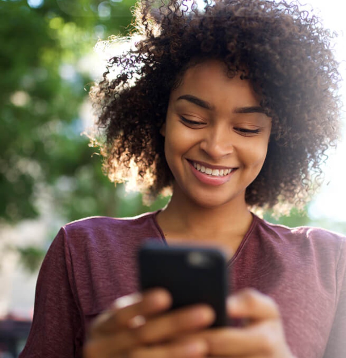 Woman smiling while looking at her phone outdoors